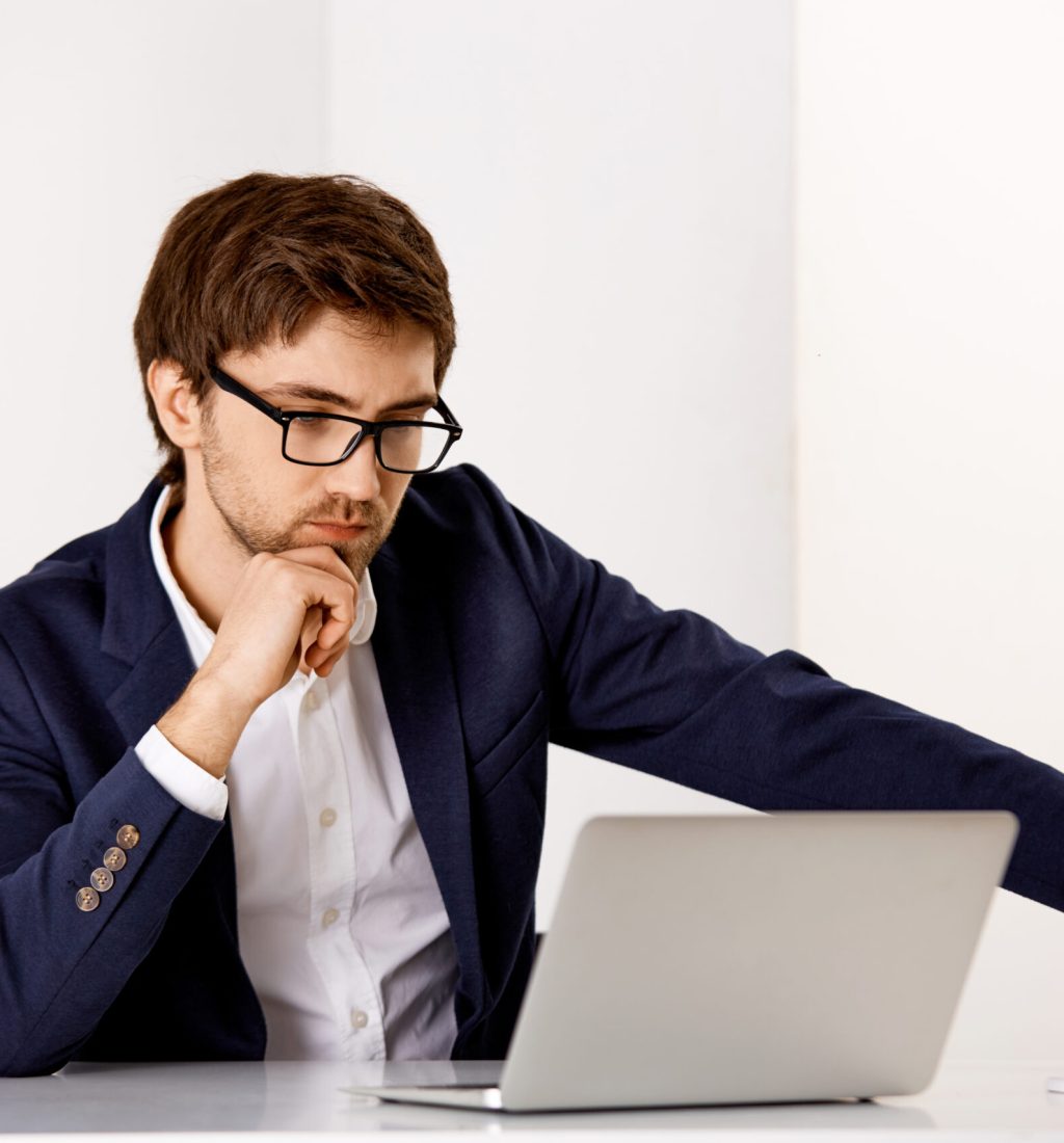 Handsome confident young businessman wearing glasses and sitting at the office desk. Isolated on white background.